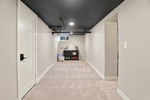 A basement room showcasing fresh carpeting, a modern black ceiling, and decorative furniture, suitable for multiple purposes.