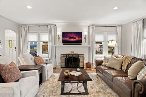 Spacious living room with plush sofas, a rustic wooden coffee table, and a fireplace, illuminated by natural light from large windows.