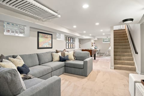 A spacious lounge area with a gray sectional couch, decorative pillows, and artworks on the walls.