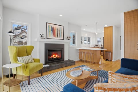A modern living room with a cozy fireplace, green accent chair, and stylish furniture, illuminated by natural light.