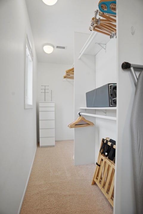 A bright and spacious walk-in closet featuring white walls, a six-drawer chest, wooden hangers, and soft beige carpeting.