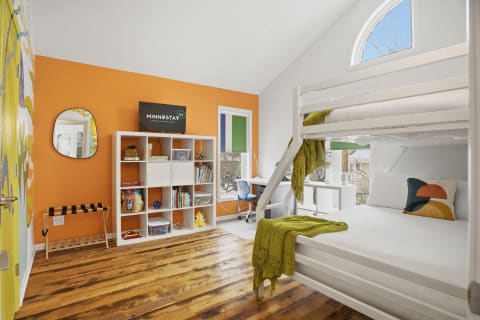 Bright children's bedroom with orange accent wall, bunk bed, bookshelf, and desk.