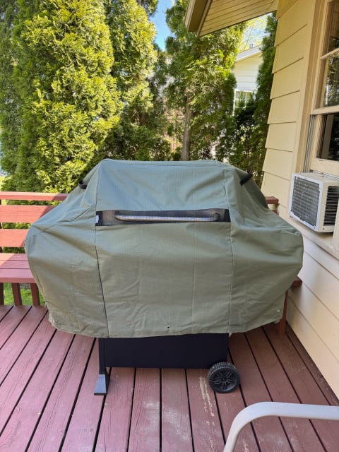 A green-covered grill on a wooden deck with trees in the background.