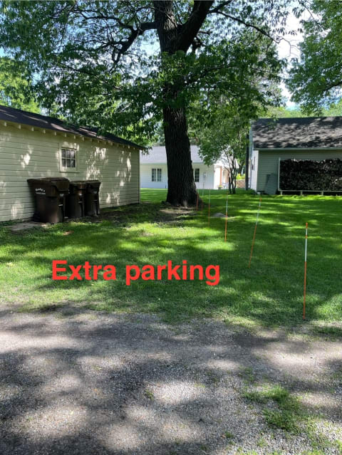 Grassy area marked for extra parking with stakes and nearby buildings.
