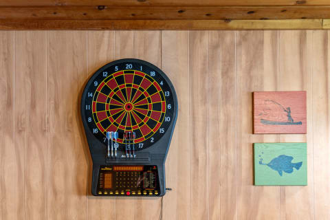 A wall with an electronic dartboard and two wooden panels, one showing a fisherman and the other a fish.