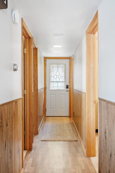 A well-lit hallway featuring wooden trim and a closed white door at the end.