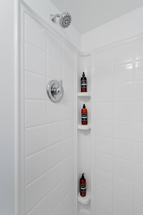 Interior of a modern shower with white tiles and hair care products on a shelf.