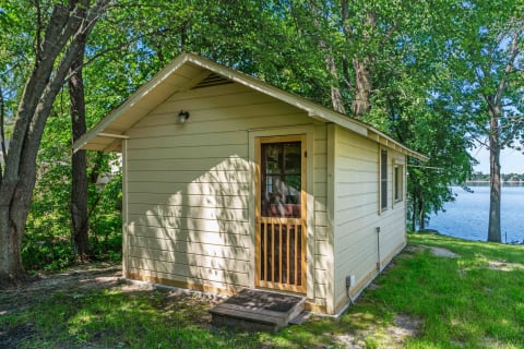 A small yellow cabin adjacent to a lake, surrounded by trees.