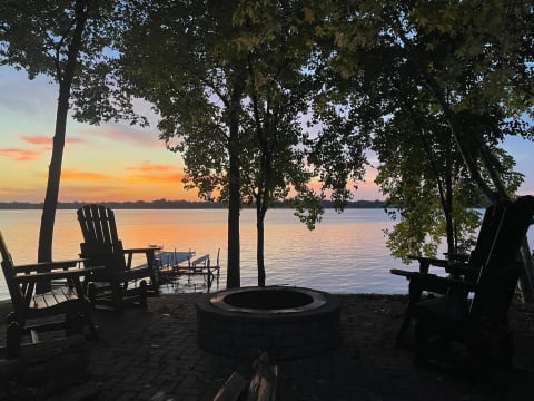Lakeside view with chairs and a fire pit during sunset.