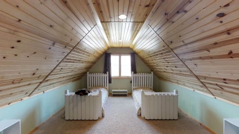 An attic bedroom with sloped wooden ceilings, two white beds, and a plush bear on one bed.