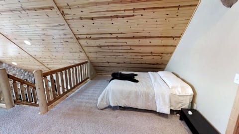 Cozy attic bedroom with wooden ceiling, a bed, and a wooden railing.