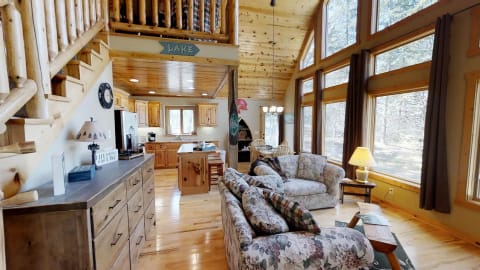 Interior view of a cozy rustic cabin featuring floral sofas, wooden furniture, and large windows.