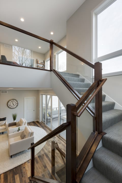 Interior view of a staircase with glass railing and carpet, leading to a modern living space.