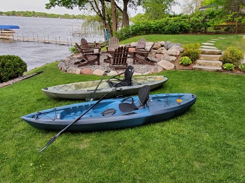 Two parked kayaks on green grass by a lake with a wooden dock in the background.