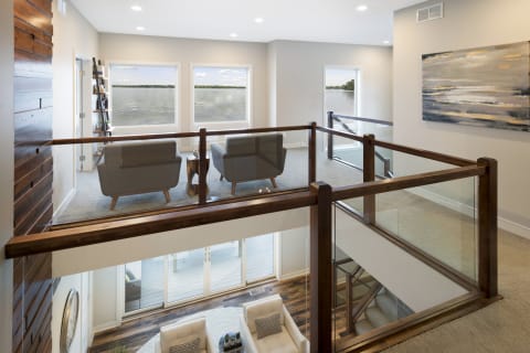Open loft area in a modern home featuring gray armchairs and large windows overlooking the water.