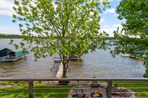 Lakeside view featuring a green tree, docks, and a fire pit.
