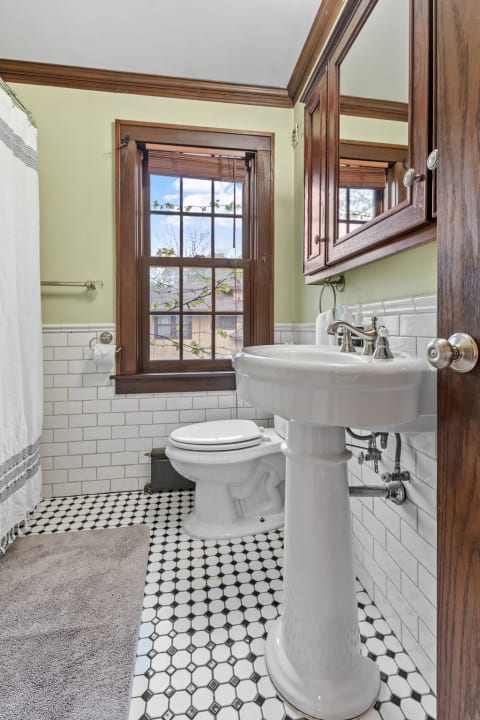 A stylish bathroom featuring a pedestal sink, toilet, and hexagonal tiled floor under a bright window.
