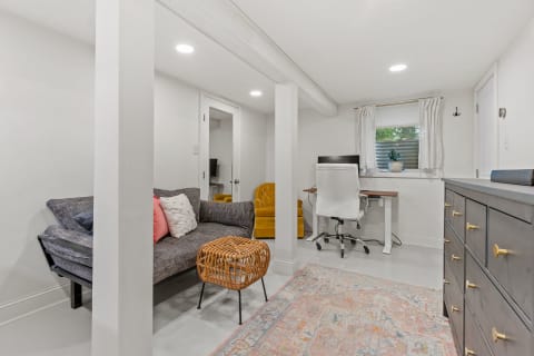 Modern basement room with a sofa, yellow armchair, desk, and decorative rug.