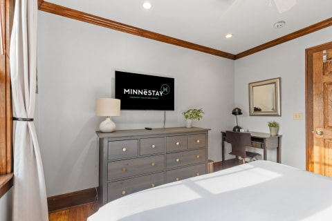 Stylish bedroom with a gray dresser, TV, and a cozy workspace.