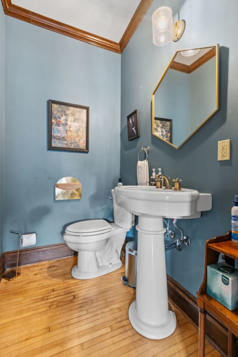 Small bathroom with blue walls, a white pedestal sink, and wooden accents.