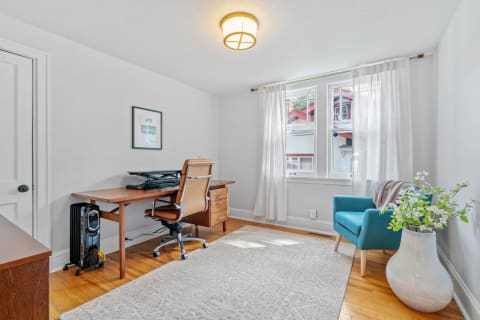 A cozy home office with a wooden desk, ergonomic chair, and turquoise armchair by the window.