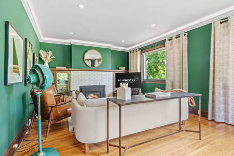 A stylish living room featuring a green wall, beige sofa, and a vintage fan.