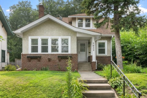 A welcoming house with a brick and stucco exterior, steps leading to the front door, and lush greenery.