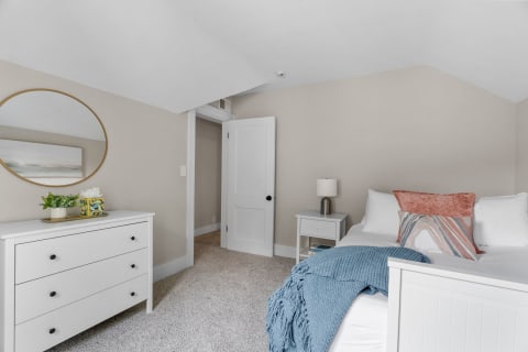 A well-decorated bedroom with a bed, dresser, and soft color scheme.