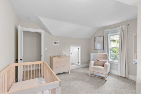 A softly decorated nursery room with a crib, rocking chair, and large window.