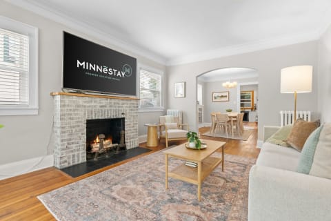 Cozy living room with a fireplace and modern decor, featuring a television displaying the MINNēSTAY logo.