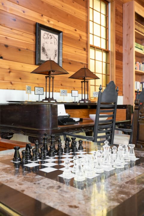 A chess set on a marble table in a cozy wooden room with vintage decor and a typewriter in the background.