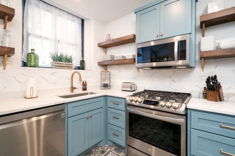 Modern kitchen featuring blue cabinets, a stainless steel oven, and wood shelves with decorative items.