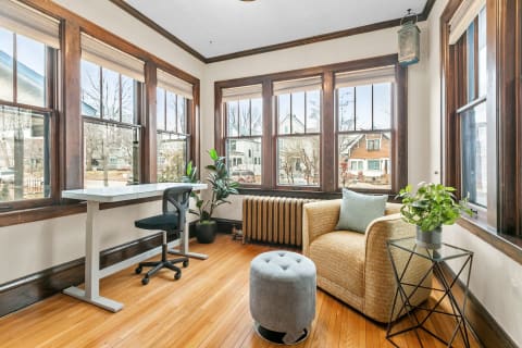 A well-lit corner of a room with a desk, chair, armchair, and plants.