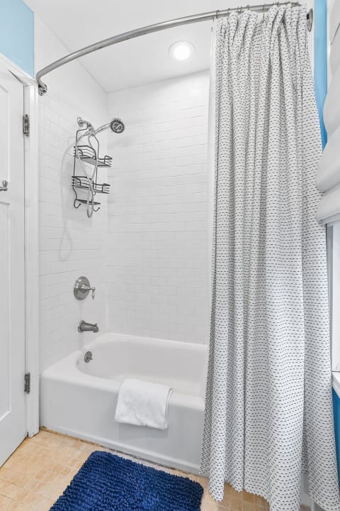 Cozy bathroom with white bathtub, gray patterned shower curtain, and navy blue bath mat.