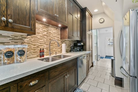 A contemporary kitchen with dark wooden cabinets, a light countertop, a modern sink, and an exit door framed by a blue mat.
