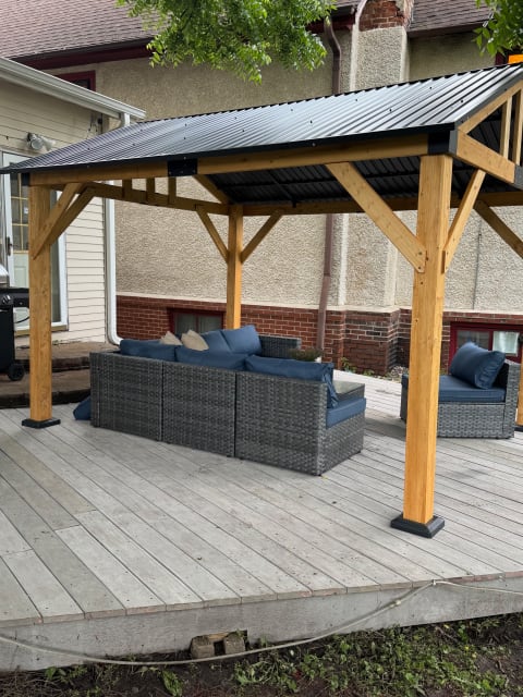Outdoor seating area beneath a wooden gazebo, featuring a wicker sectional sofa with blue cushions.