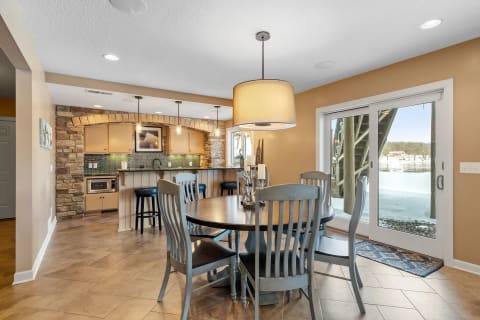 Cozy dining area with round table, colorful backsplash in kitchen and lakeside view.