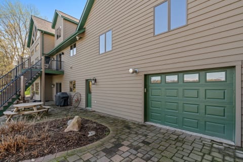 Side view of a beige and green two-story house with patio furniture and a garage.