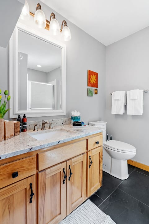 Contemporary bathroom with a light granite countertop, wooden cabinets, and decorative wall art.