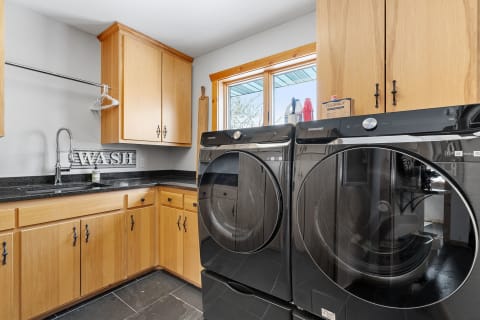 Modern laundry room featuring black washing machines, wooden cabinets, and a stylish sink.