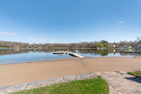 Lakeside view featuring a sandy beach and a wooden dock under a clear blue sky.