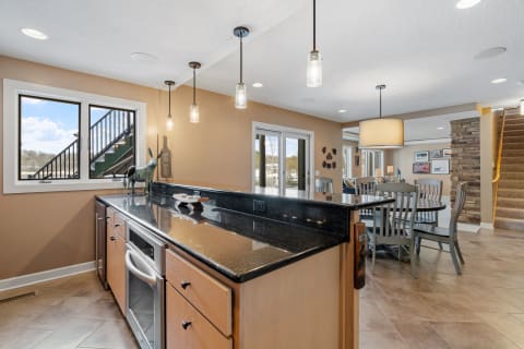 A contemporary kitchen featuring a black granite countertop, pendant lighting, and a view of a staircase.