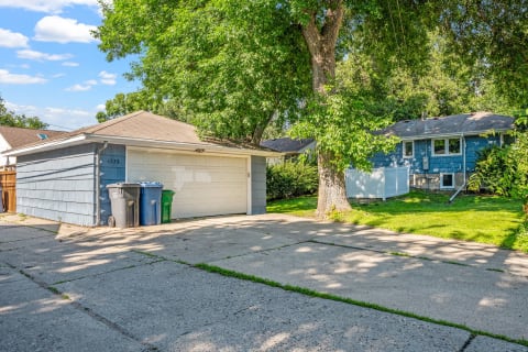 A driveway leading to a blue garage, with trash bins and green grass nearby.