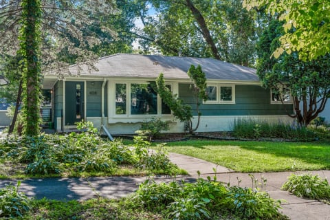 One-story green house with a well-kept front yard and pathway.