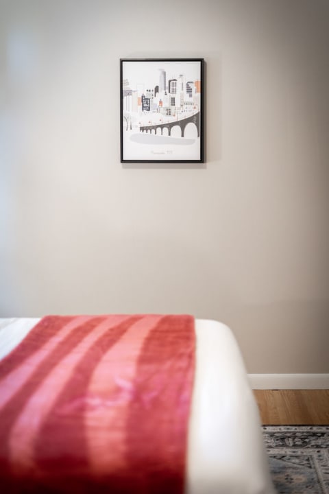 Cozy bedroom featuring a framed skyline artwork and a red striped blanket on the bed.
