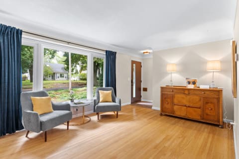 A cozy living room with gray chairs, a round table, and a wooden sideboard illuminated by soft lamps.