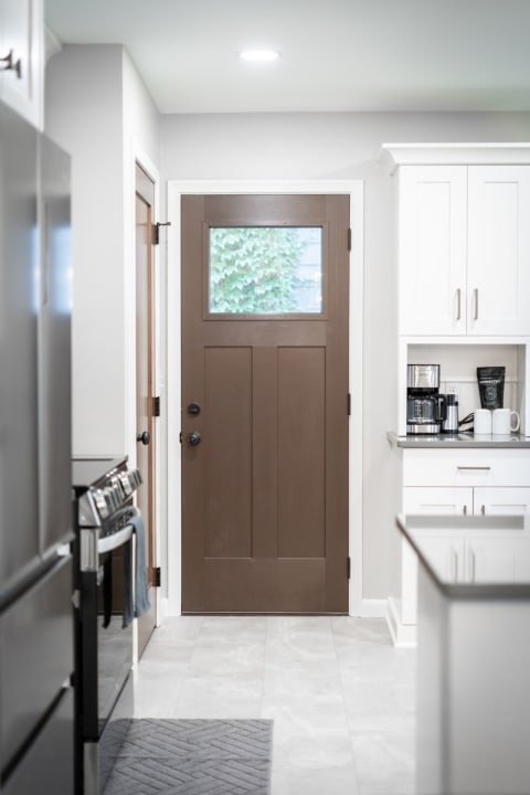 Interior of a kitchen showing a brown door and contemporary white cabinetry.