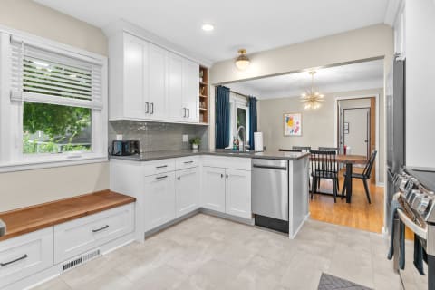 Modern kitchen featuring white cabinets, a wooden bench, and a dining area.