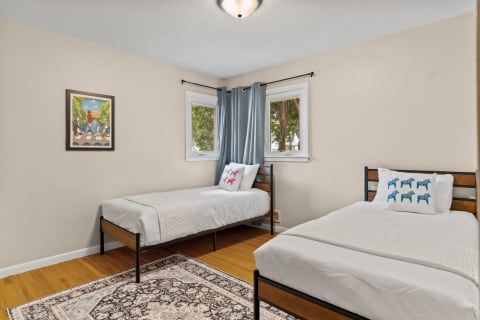 A well-decorated bedroom with two twin beds, blue curtains, and artwork on the wall.