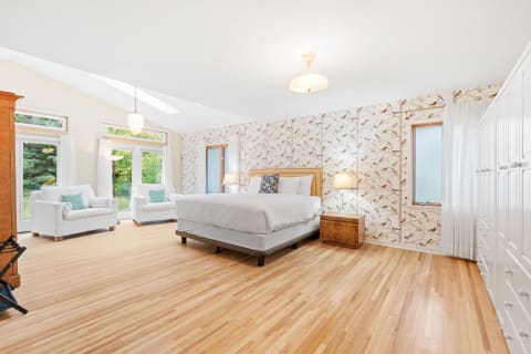Modern bedroom featuring a queen-sized bed, bird-themed wallpaper, and white armchairs.